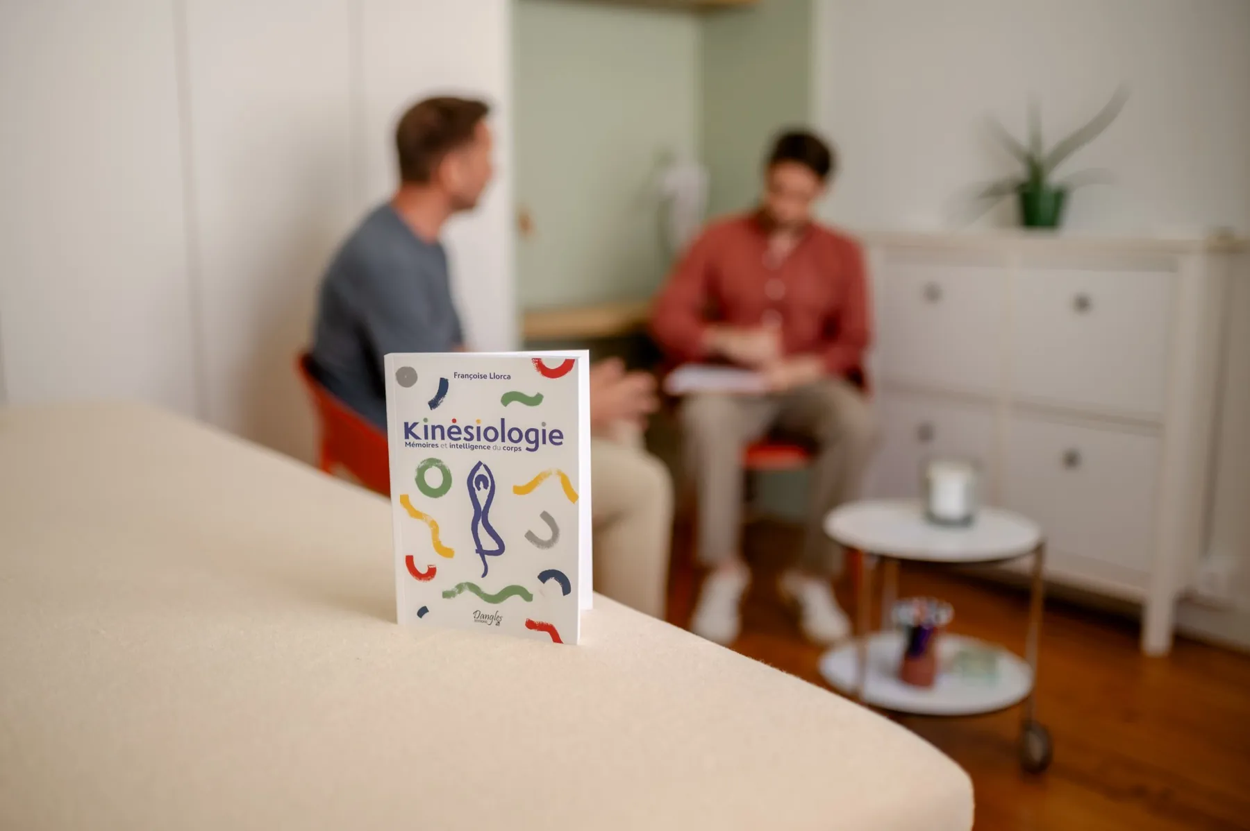 Le livre « Kinésiologie » posé sur la table de séance, un échange en arrière-plan.